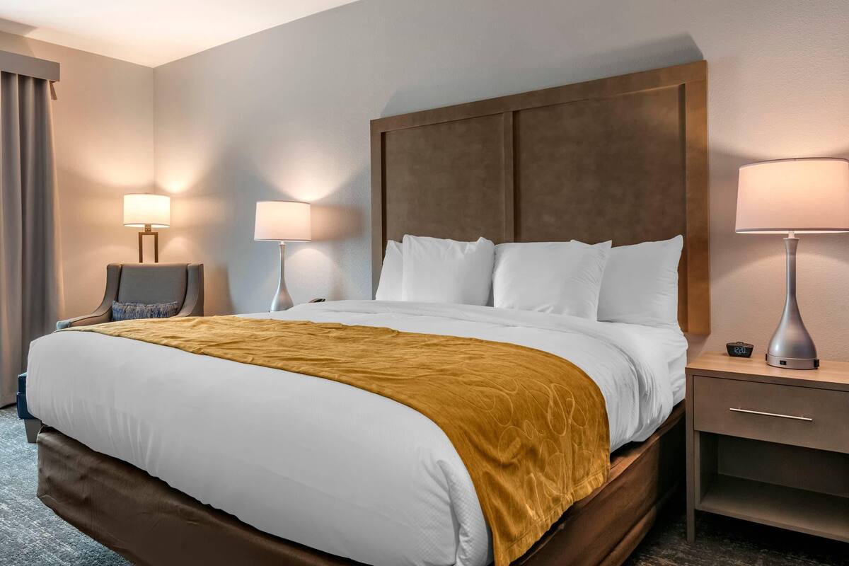Una habitación de hotel con una cama grande, dos lámparas de noche, una mesita de noche y una silla.
