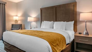 A hotel room with a large bed, two bedside lamps, a nightstand, and a chair.