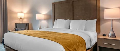 A hotel room with a large bed, two bedside lamps, a nightstand, and a chair.