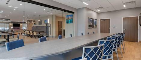 A conference room with a long table, blue chairs, and a glass partition.