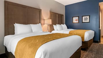 A hotel room with two beds, a brown headboard, a lamp, and two framed pictures on the wall.