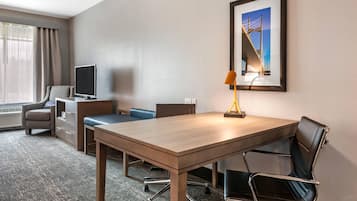 Habitación de hotel con un escritorio de madera, una silla de cuero negro, televisor, lámpara y un cuadro en la pared.
