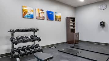 A gym with dumbbells, a bench, mats, a clock, and artwork on the wall.