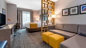 Habitación de hotel con cama, sofá, escritorio, televisor, lámpara de escritorio, silla y un separador decorativo.