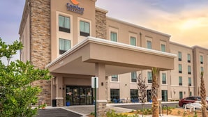 Edificio de Comfort Inn & Suites con entrada cubierta, múltiples ventanas y un estacionamiento con coches y palmeras.