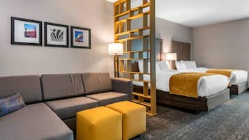 Habitación de hotel con sofá, otomanas, cama con cabecera y cuadros en la pared.
