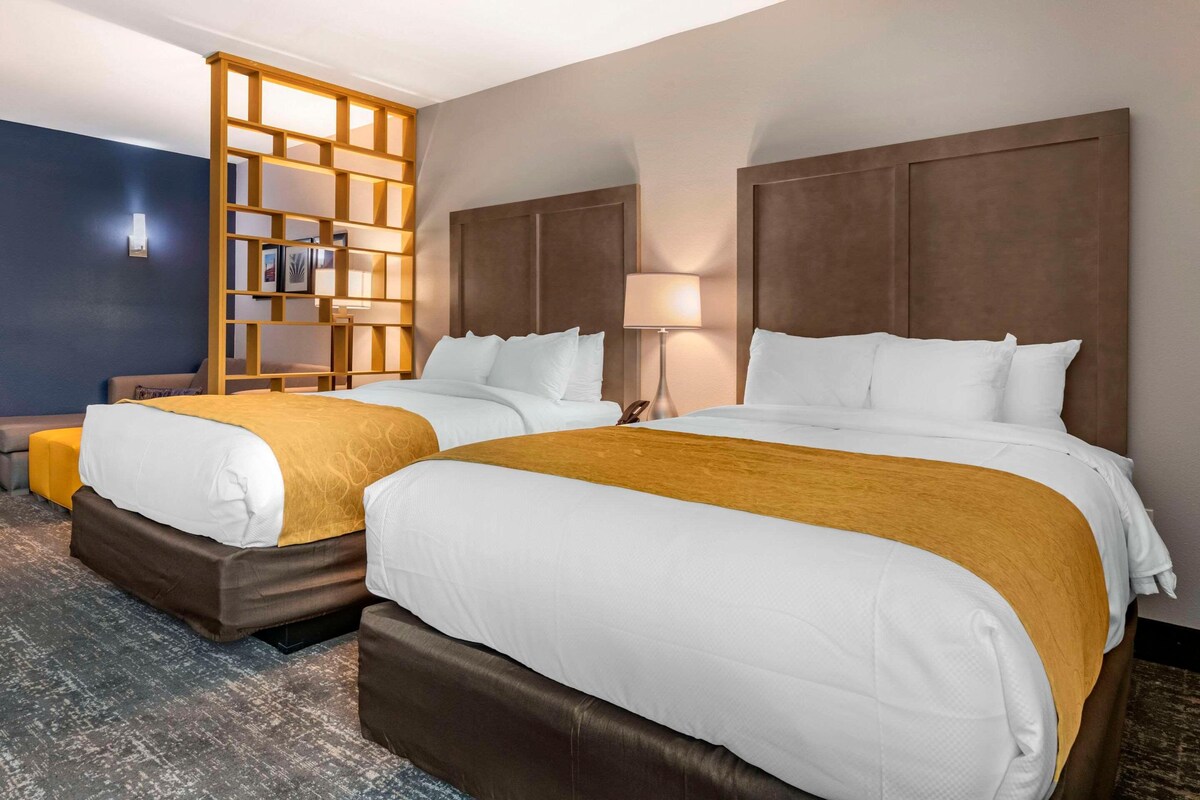 Habitación de hotel con dos camas, un separador de madera con estantes, un escritorio y una silla.