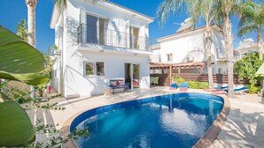 Una casa bianca a due piani con piscina, circondata da palme e un pontile in legno.