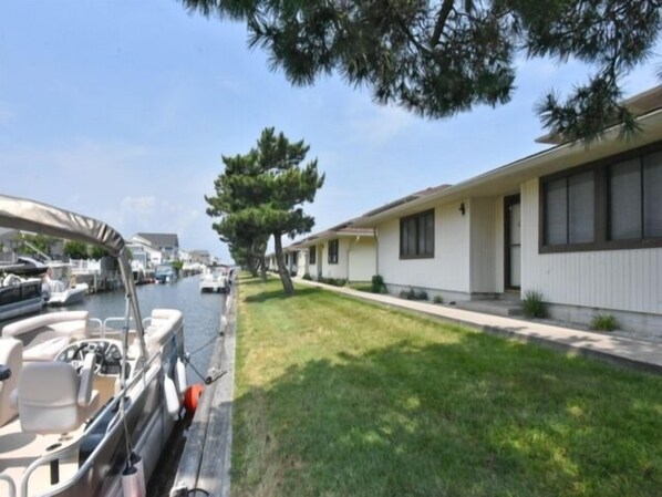 A row of single-story houses with a grassy lawn and a dock with boats.