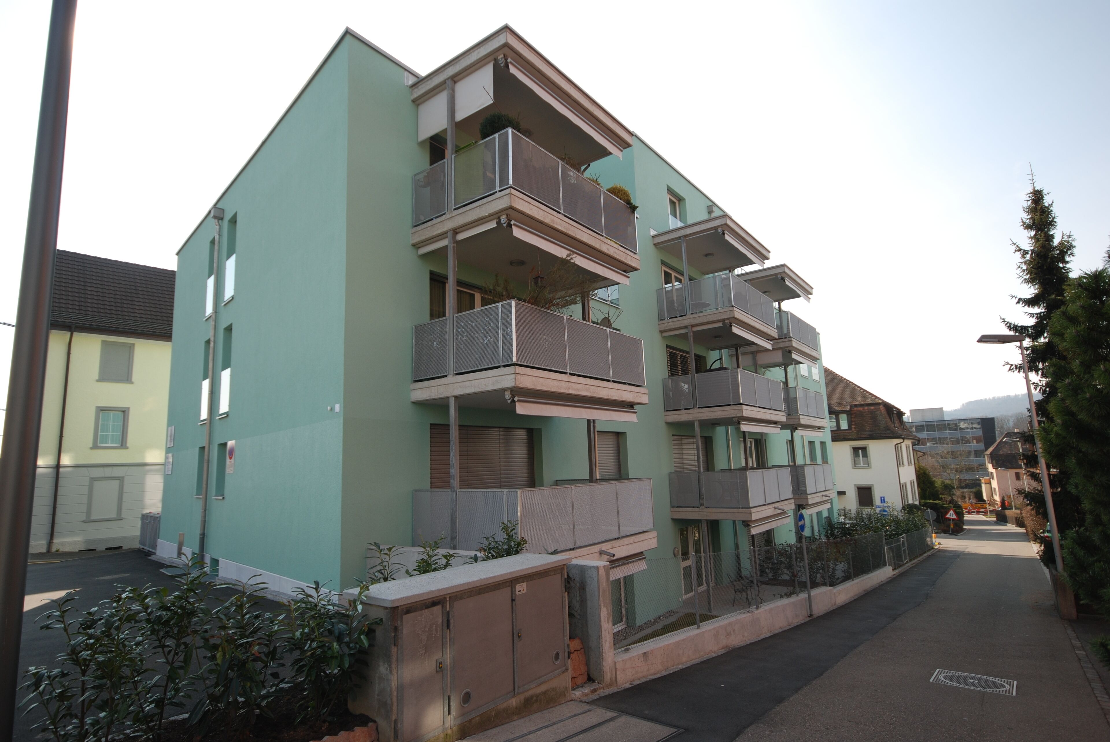 A multi-story residential building with balconies, a gated entrance, and a narrow street.