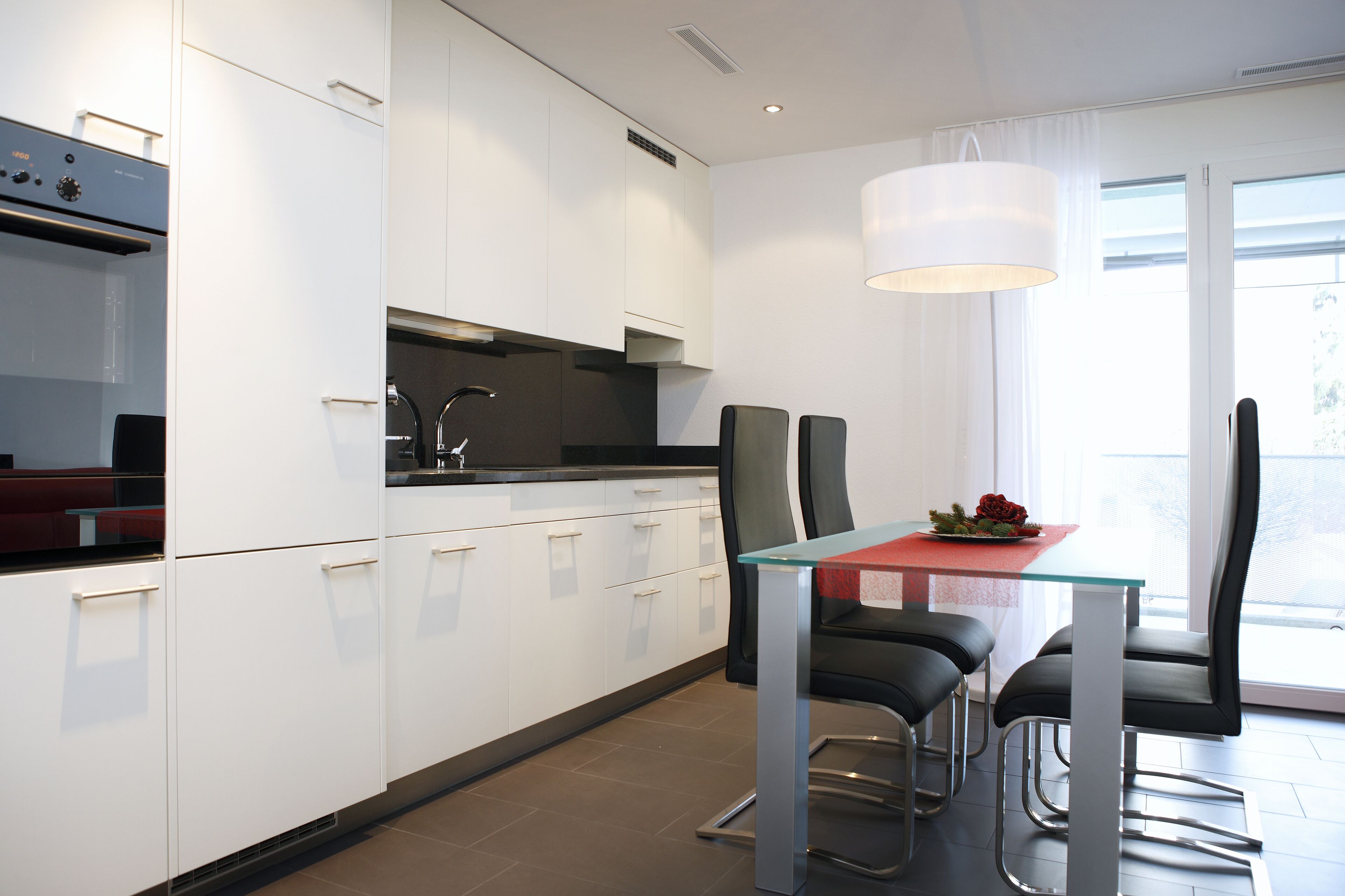 A modern kitchen with white cabinets, a glass-top table, and black chairs.