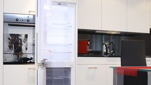 Eine moderne Küche mit weißen Schränken, einem Einbauofen und einem Esstisch mit Glasplatte und rotem Tischläufer.