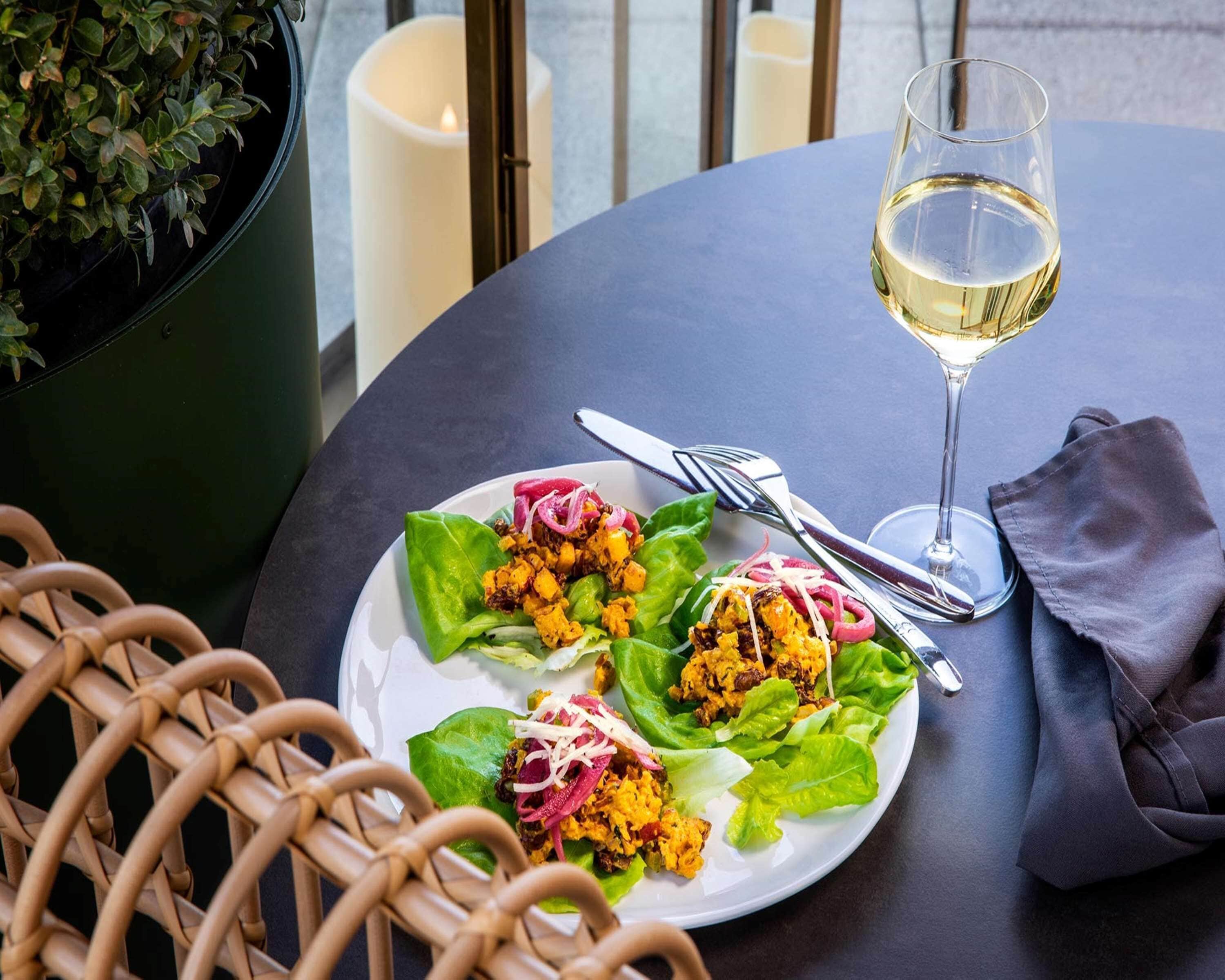 A table with a plate of food, a glass of white wine, and cutlery.