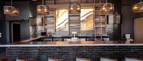 A bar area with a long counter, multiple hanging light fixtures, and bar stools.