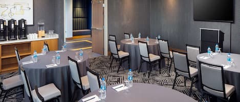 A conference room with round tables, chairs, water bottles, and a coffee station.