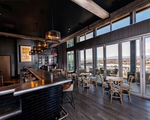 A modern bar area with a long counter, multiple seating options, and large windows offering a view of the cityscape. - Hyatt Place Harrisonburg (Harrisonburg)