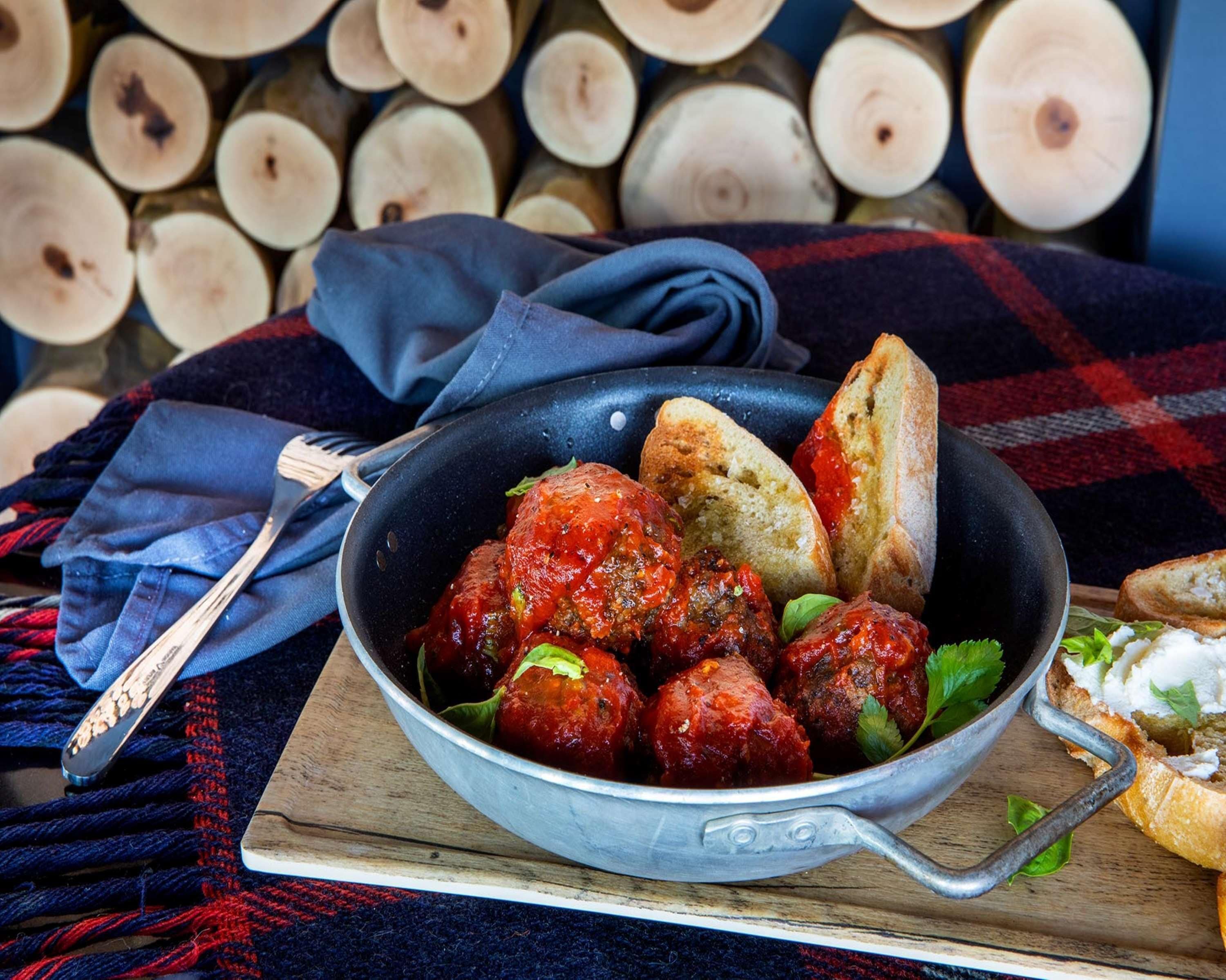 A bowl of meatballs with sauce and bread on a wooden board.