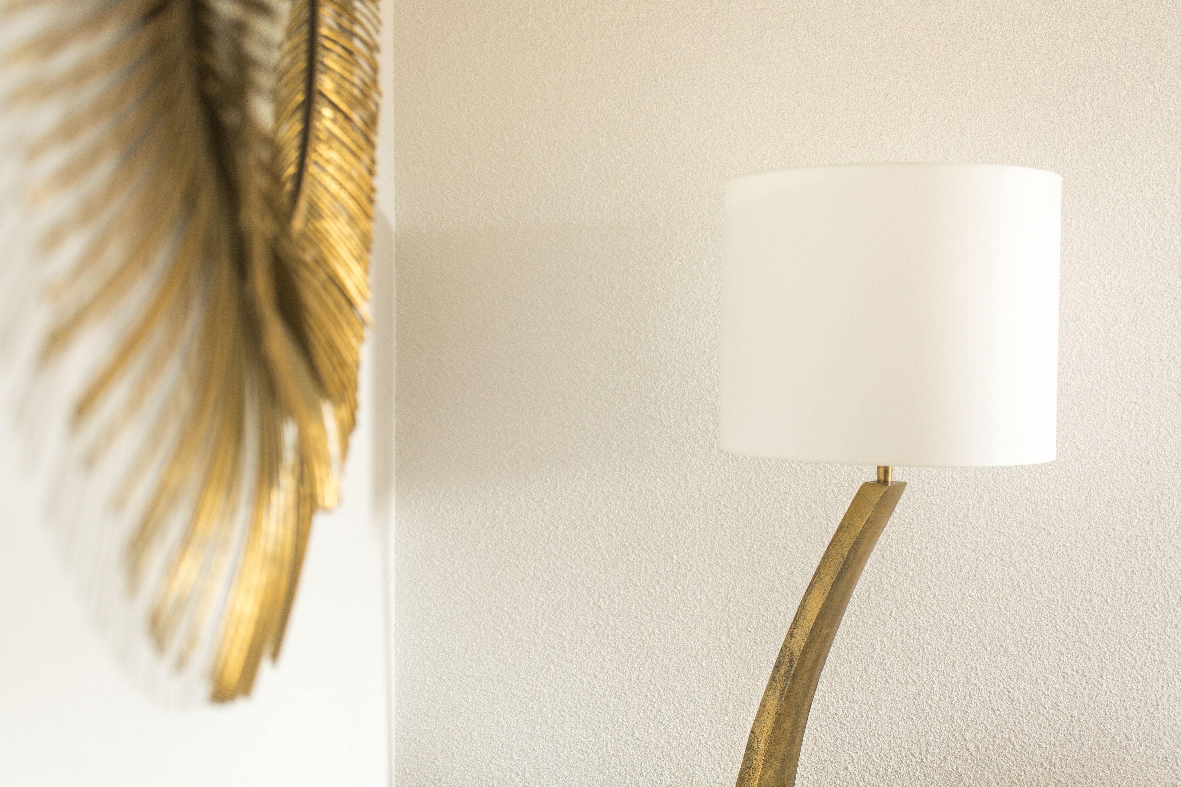 Une lampe murale avec un abat-jour blanc et un pied incurvé doré.