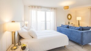 Une chambre à coucher avec un lit, un canapé bleu, deux lampes de chevet, une fenêtre avec des rideaux et un miroir fixé au mur.