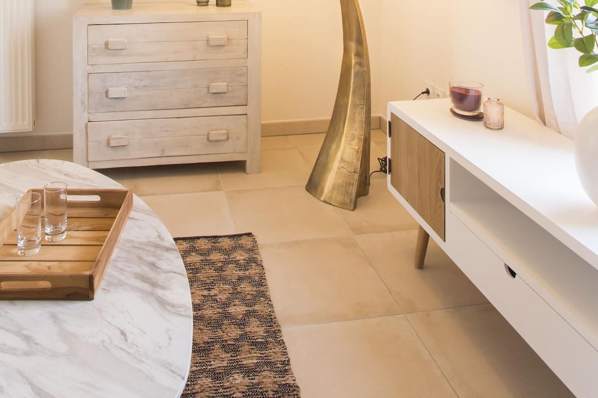 A modern bathroom with a round mirror, a white vanity, a floor lamp, and a potted plant.