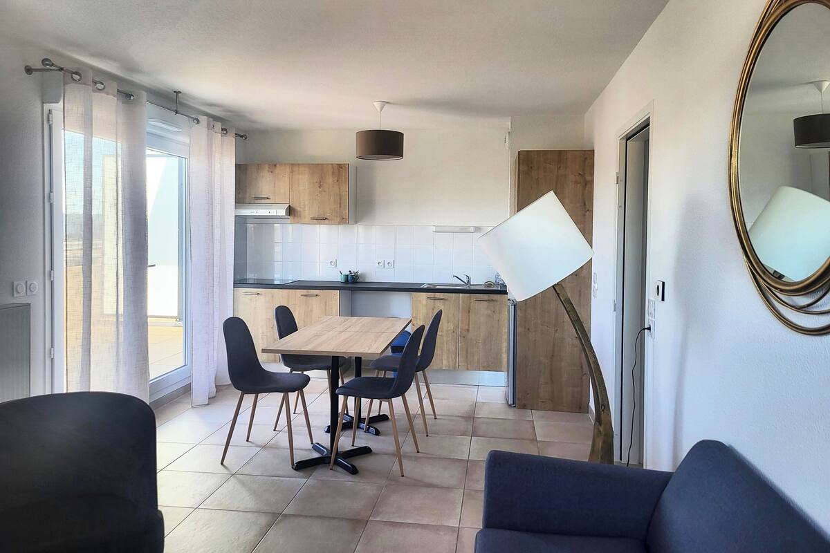 A modern kitchen with wooden cabinets, a black countertop, and a dining area with a wooden table and black chairs.