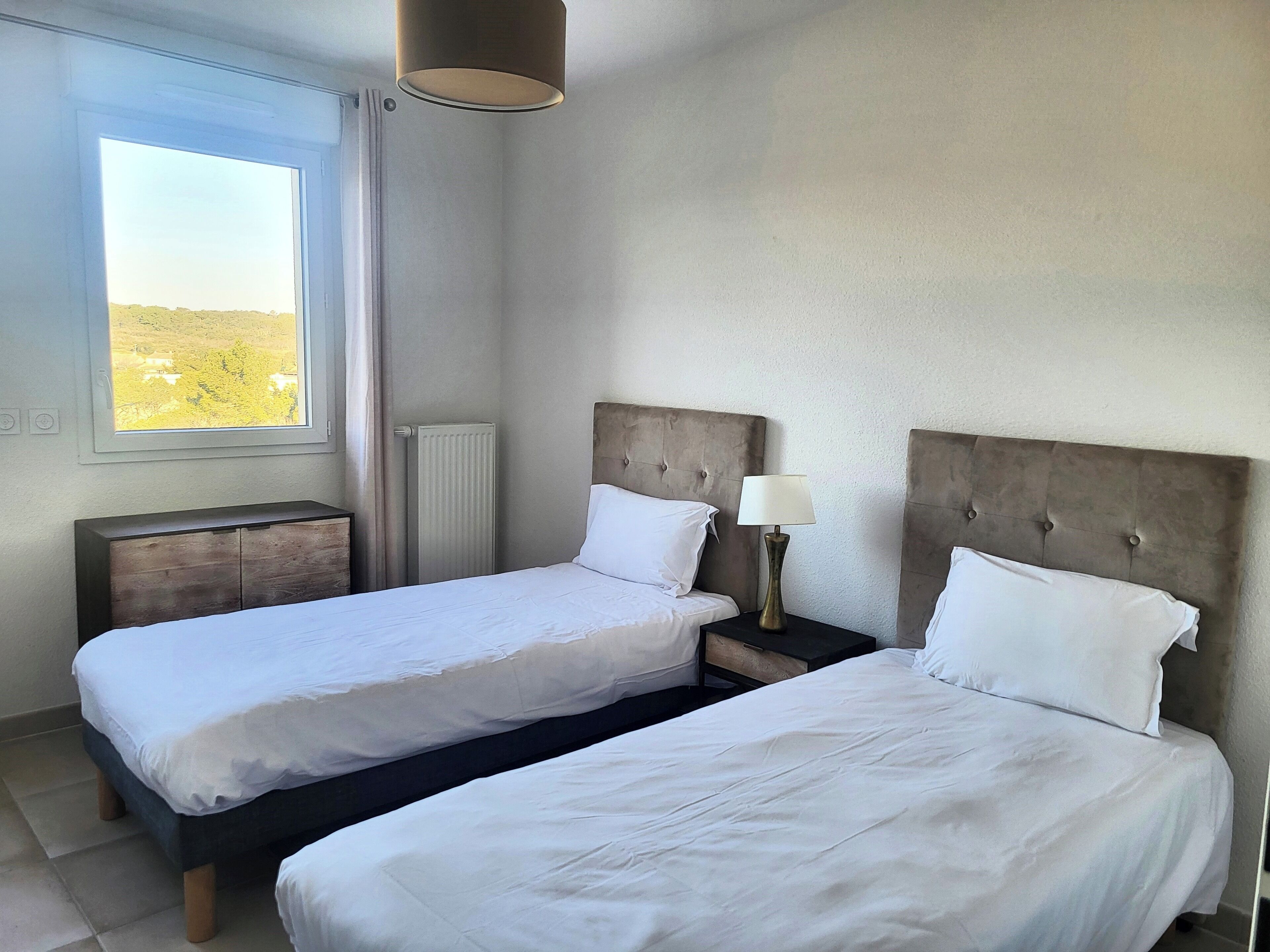 Une chambre d’hôtel avec deux lits, une fenêtre donnant sur un paysage agréable, un radiateur et une lampe de chevet.