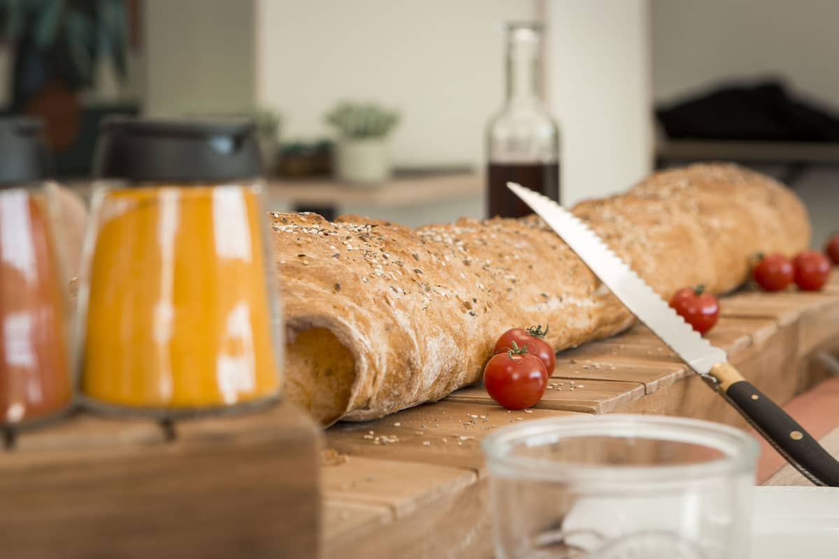 A loaf of bread on a wooden cutting board with a knife and tomatoes nearby.