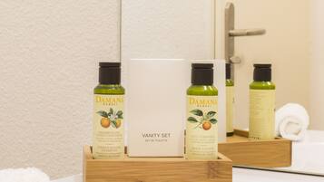 Un plateau en bois contenant trois flacons de shampoing et de lotion pour le corps à la fleur d’oranger Damana, ainsi qu’une trousse de toilette avec un miroir et une serviette.