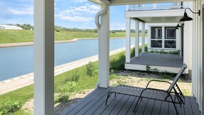 Una terraza techada al aire libre con vista a un lago, un pequeño edificio con una ventana y una silla.