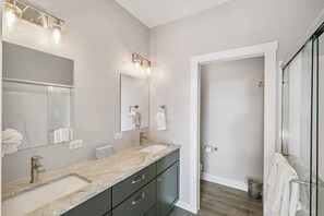 Un baño moderno con dos lavamanos, un espejo grande y una cabina de ducha con mampara de vidrio.