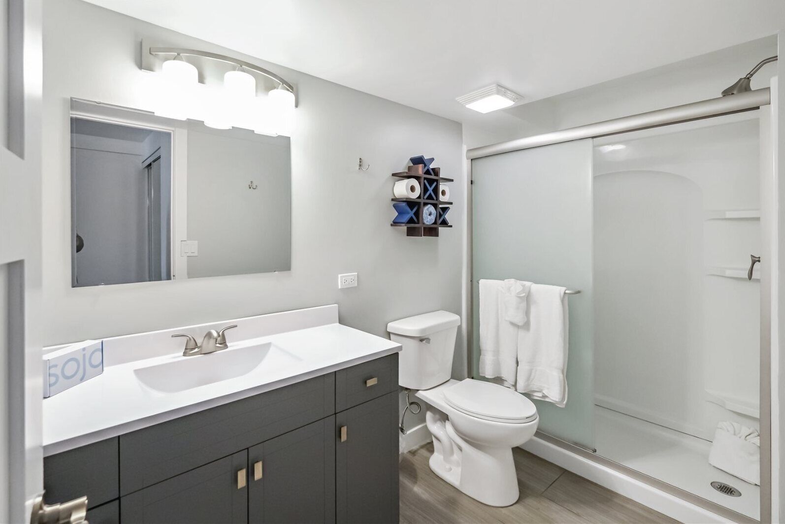 Un baño moderno con lavamanos blanco, muebles oscuros, inodoro y cabina de ducha de vidrio.
