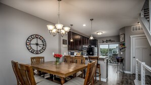 A dining area with a wooden table and chairs, a chandelier, and a wall clock. - L`il Getaway (Ottawa)
