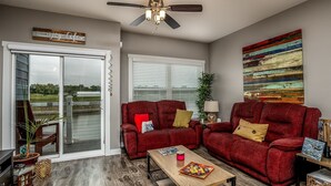 A living room with a sliding glass door leading to a balcony, a ceiling fan, and a colorful abstract painting on the wall. - L`il Getaway (Ottawa)
