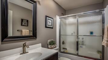 A bathroom with a white sink, a large mirror, a glass shower enclosure, and a small plant on the counter.