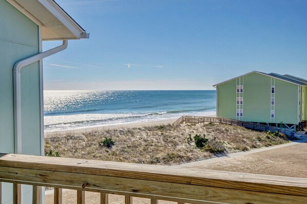 A beachfront property with a view of the ocean, a wooden deck, and a green building with windows.