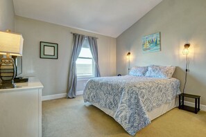 A bedroom with a bed, a nightstand, a lamp, a painting, and a window with curtains.