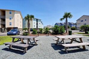 A parking area with picnic tables, a car, and residential buildings in the background.