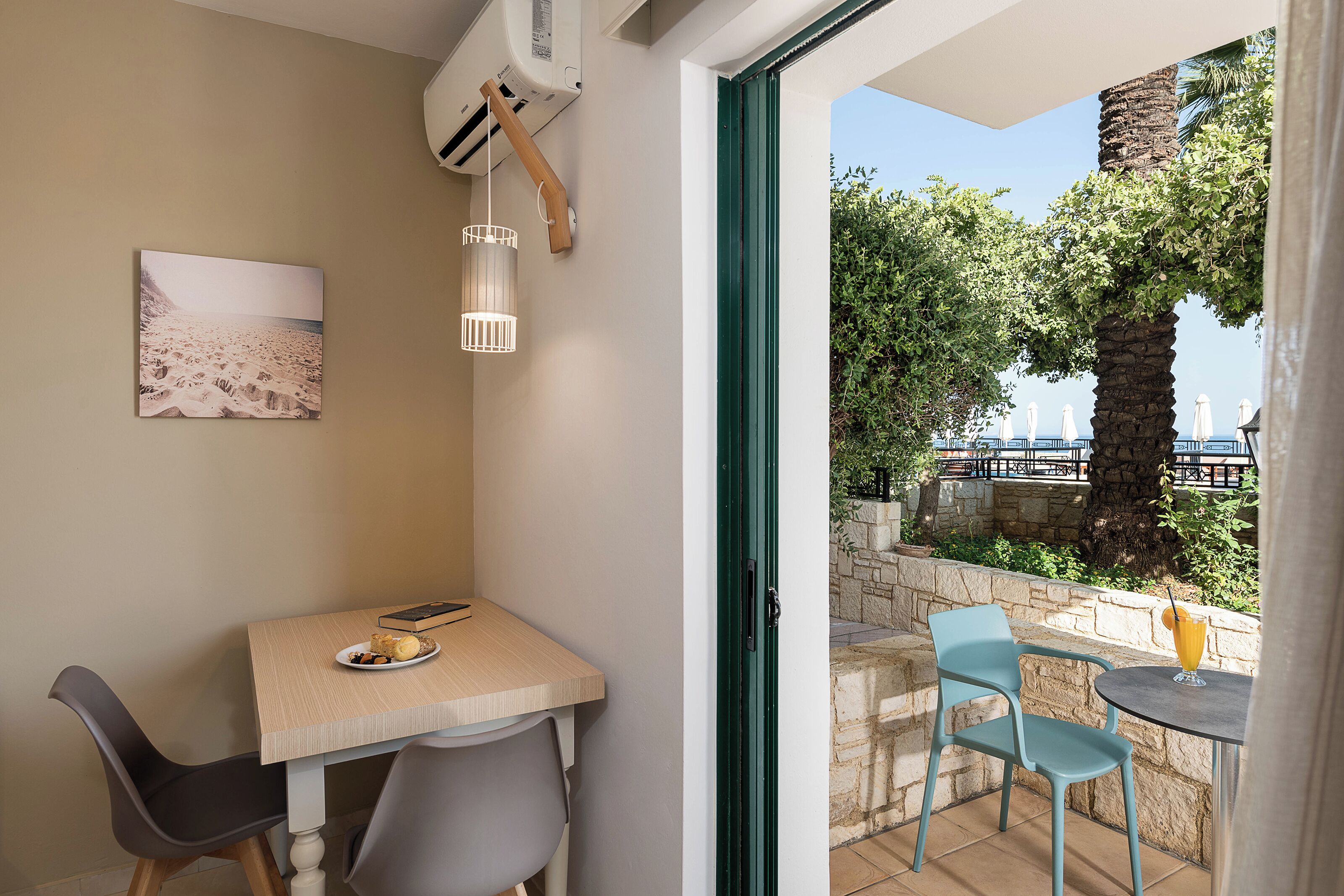 A room with a dining table, chairs, a painting, and a view of a balcony with outdoor seating and a palm tree.