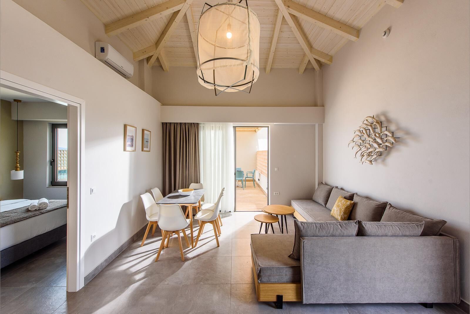 A modern living room with a sofa, dining table, and chairs. There is a ceiling fan and a window with curtains.