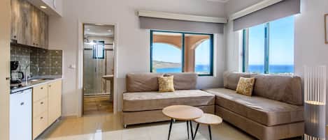 A modern living room with a beige sofa, two small tables, and a view of the sea through large windows.