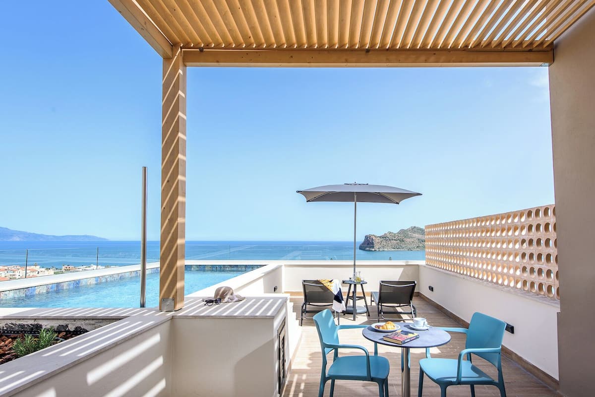 A balcony with a view of the sea, a pool, and a table with chairs.