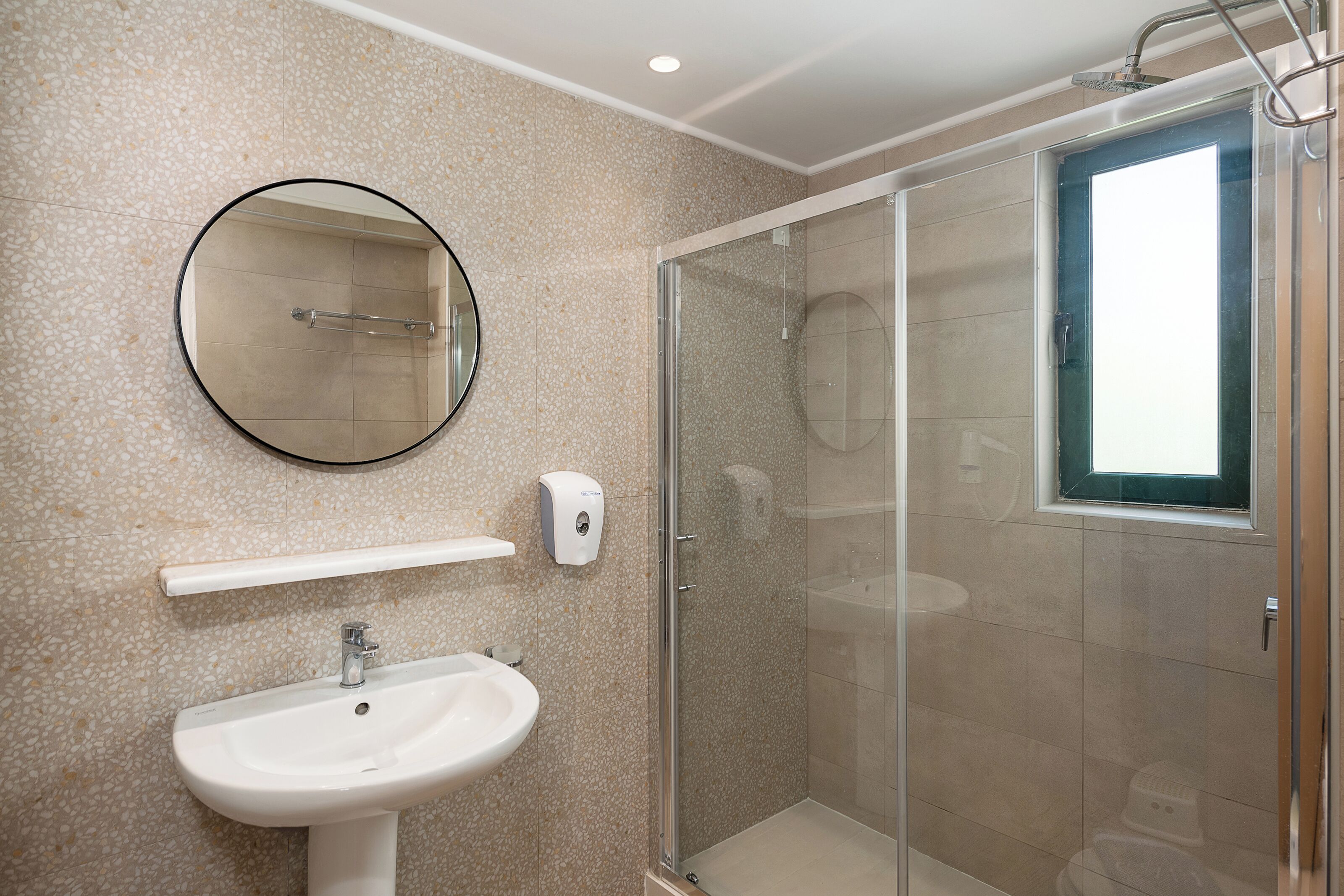 A bathroom with a glass-enclosed shower, a sink, a mirror, and a soap dispenser.