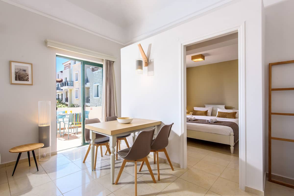 A modern hotel room with a dining area, a bed, and a view of the city.