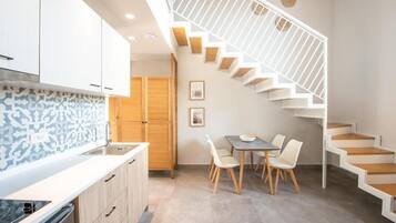 Une cuisine moderne avec des meubles blancs, un crédence décoré et un coin repas comprenant une table et des chaises.