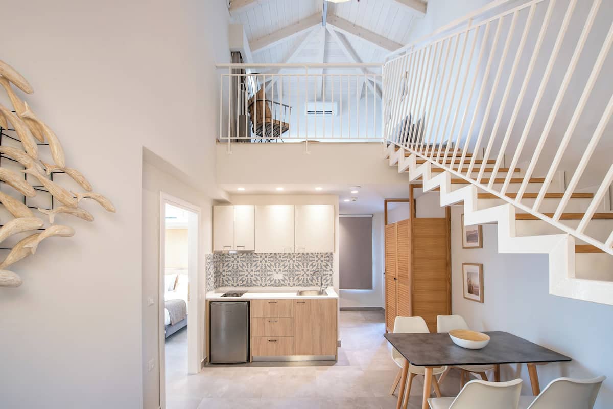 A modern kitchen with a central island, a dining area with a table and chairs, and a staircase leading to an upper level.