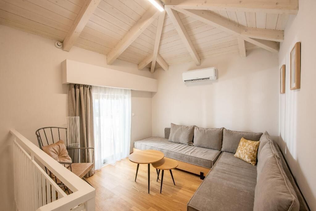 A modern living room with a sofa, a small table, and a chair. There is a staircase on the left and an air conditioning unit on the wall.