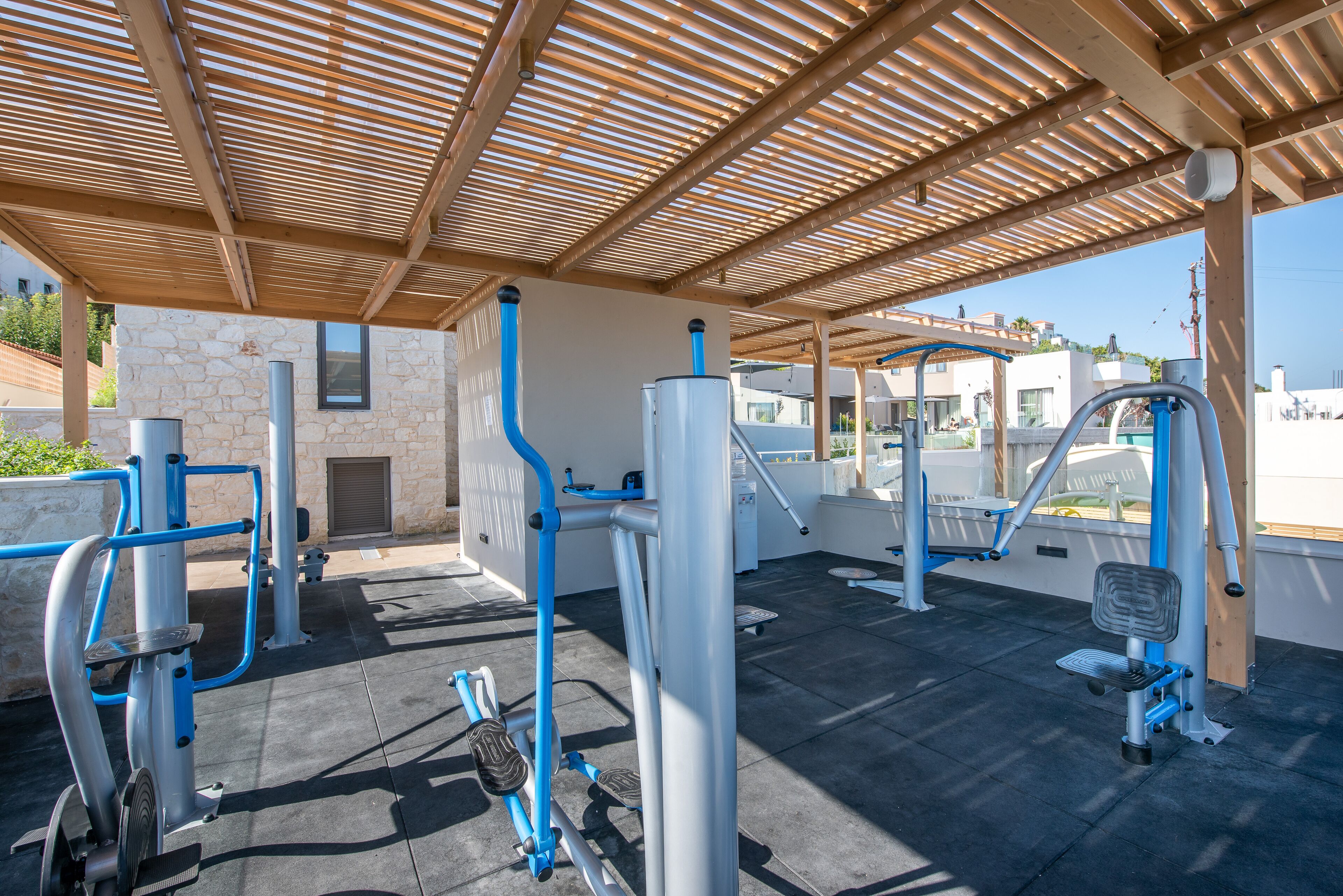 An outdoor gym with exercise equipment, a covered area, and a stone building in the background.