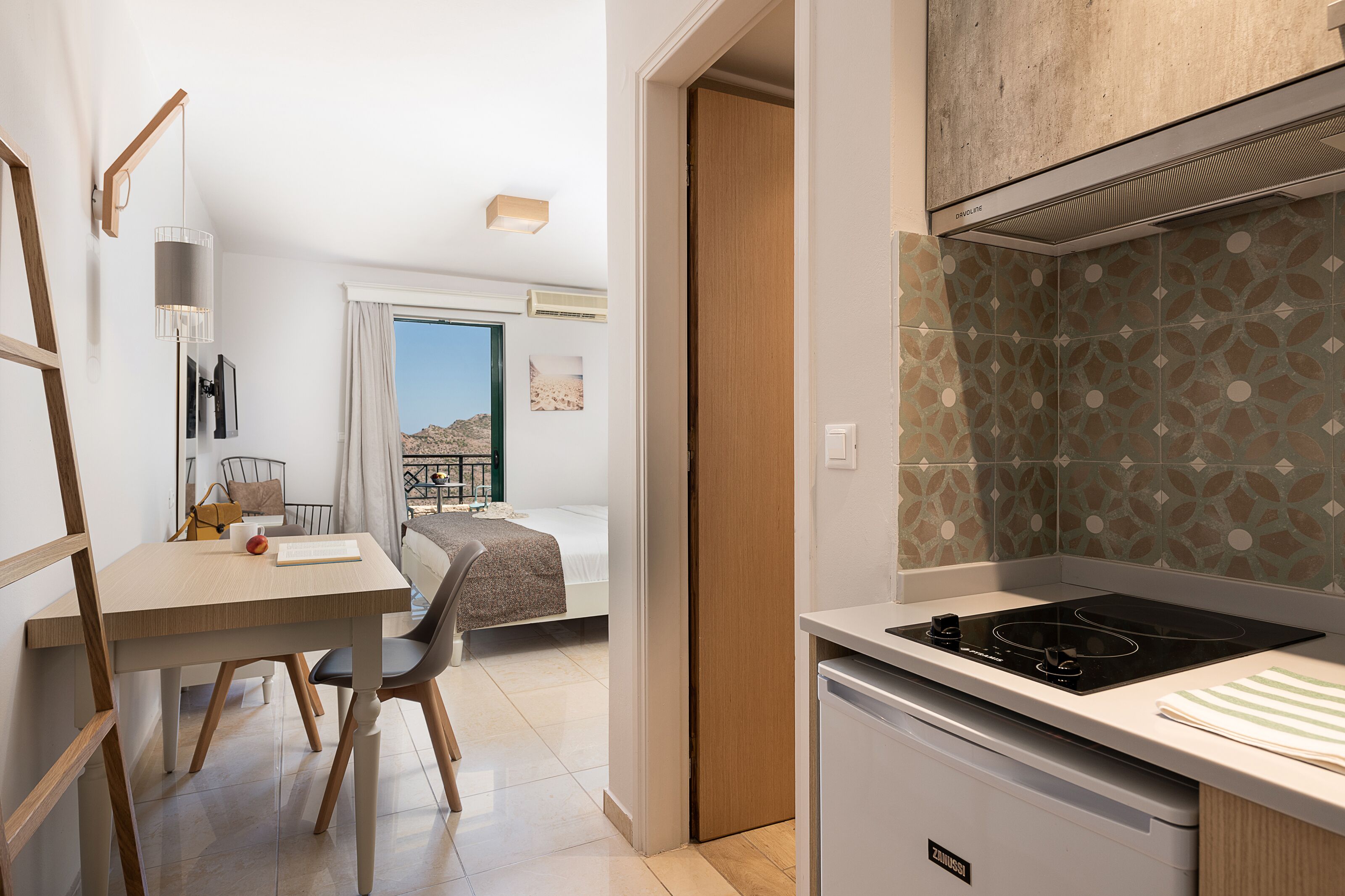 Une cuisine moderne dotée d’une cuisinière intégrée, un coin repas avec une table et des chaises, et une vue sur un balcon donnant sur un paysage désertique.