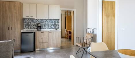 A modern kitchen with wooden cabinets, a built-in oven, and a coffee maker. There is a dining area with a table and chairs.