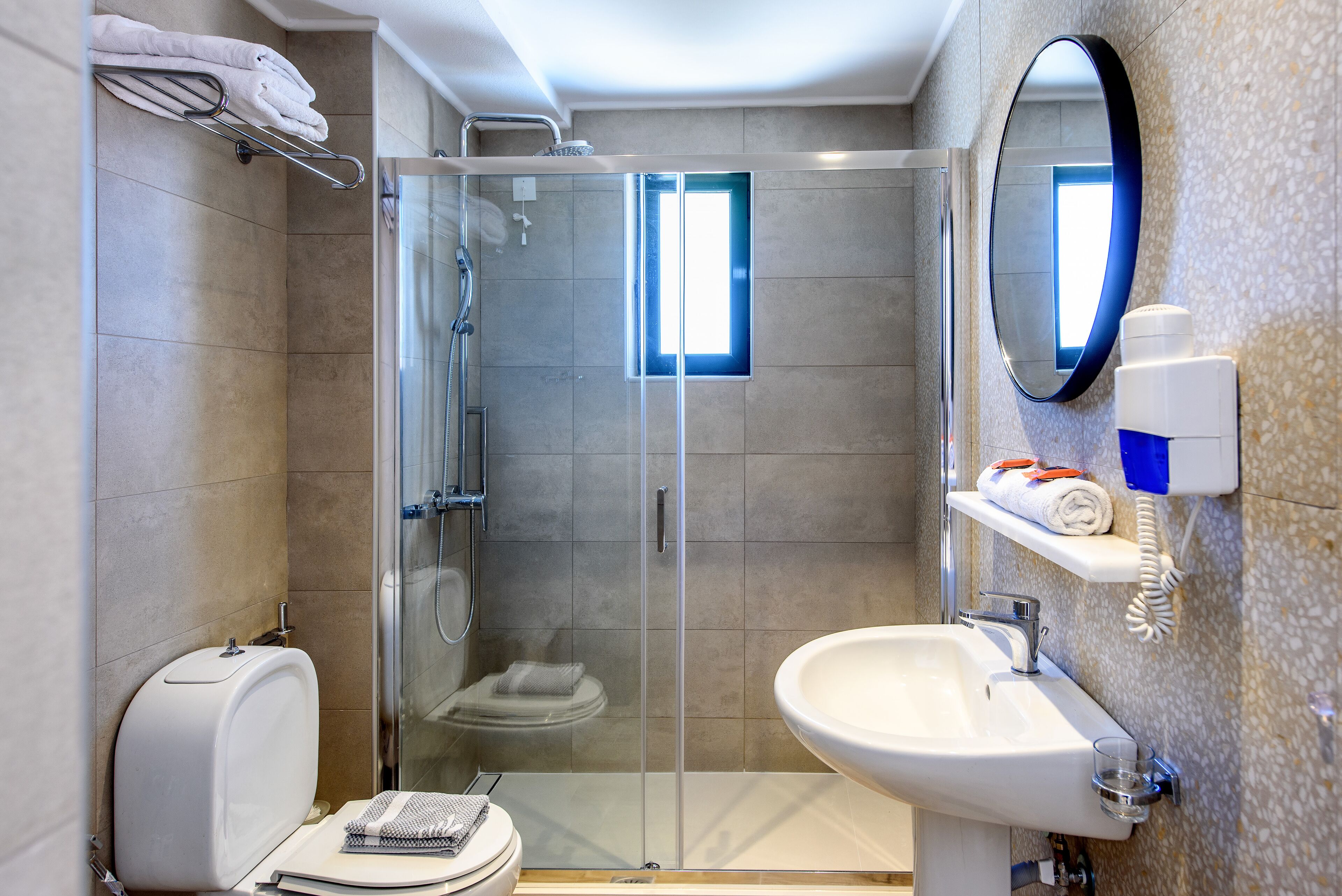 A modern bathroom with a glass-enclosed shower, a toilet, a sink, and a mirror.